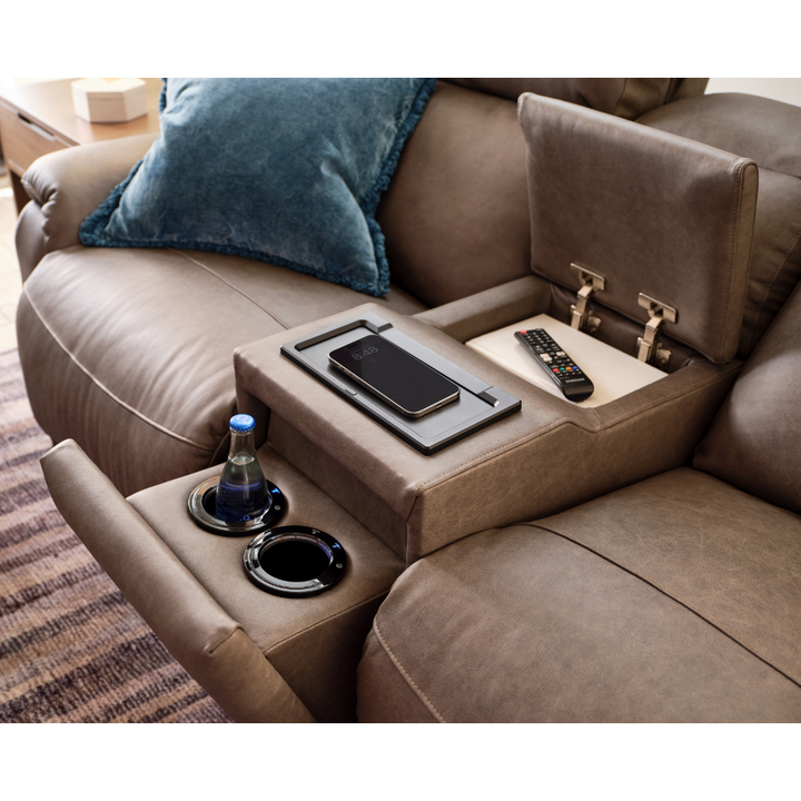 Brown sofa with a built-in tray table, phone, remote control, and bottle on a carpeted floor.