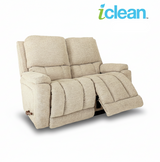 Reclining loveseat with light beige fabric, padded arms, and recline footrest